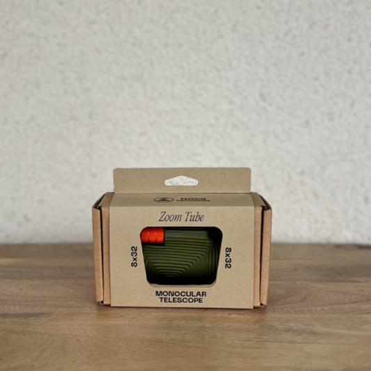 Monocular telescope in a cardboard box on a wooden surface with a neutral background