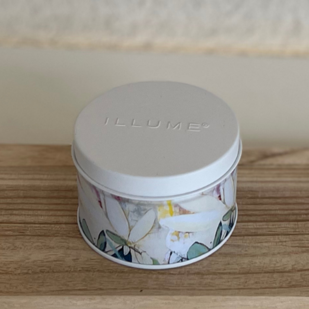 Candle tin with floral design and 'ILLUME' branding on a wooden surface