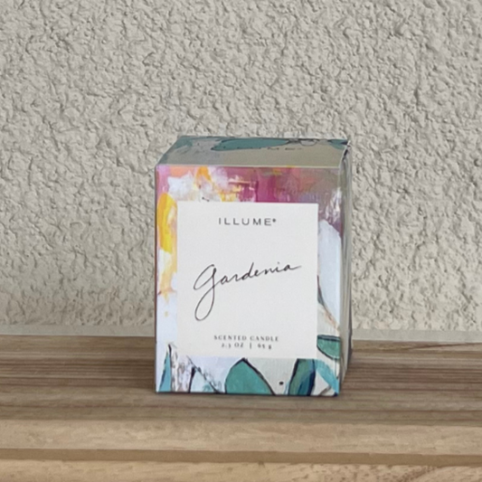 Illume Gardenia scented candle packaging on a wooden surface with a neutral wall background