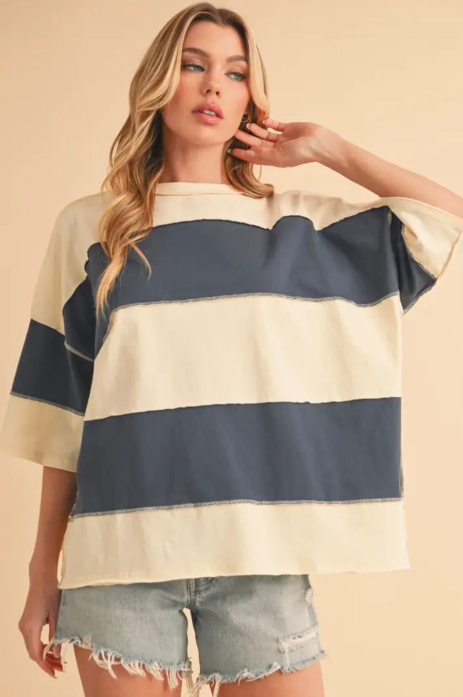 Woman wearing a beige and navy striped sweater with denim shorts on a beige background